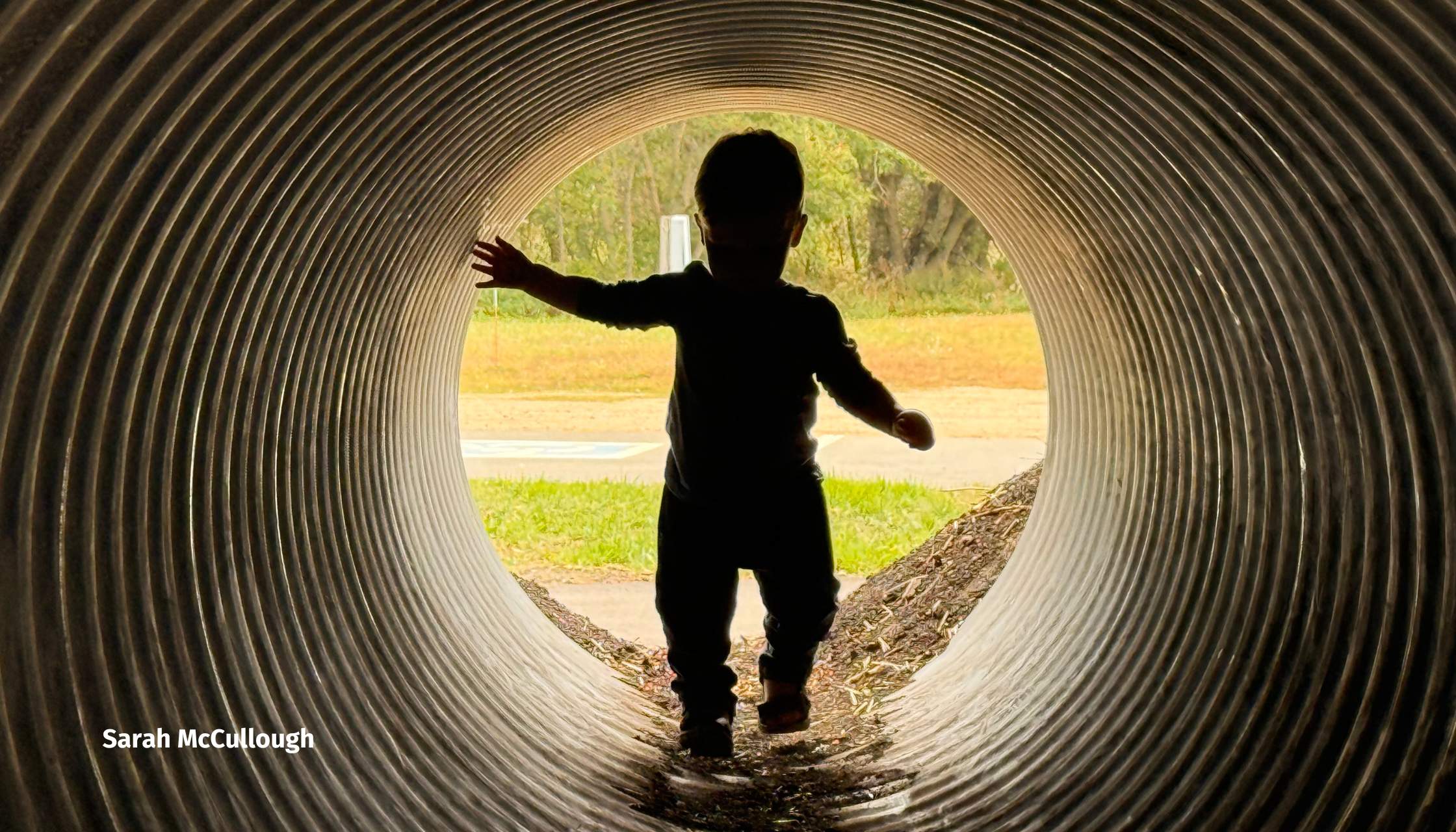 A kid walking through a metal tube.
